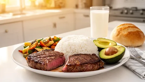 A loaded plate of sliced steak, rice, roasted vegetables and avocado with a glass of milk
