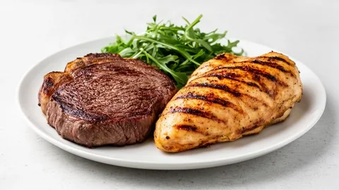 A single plate holding a thick sliced steak and a whole grilled chicken breast with a small pile of greens